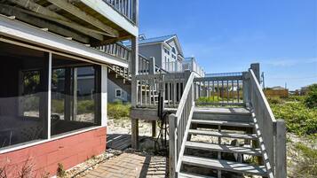A coastal house with a wooden deck and a staircase leading to a balcony.