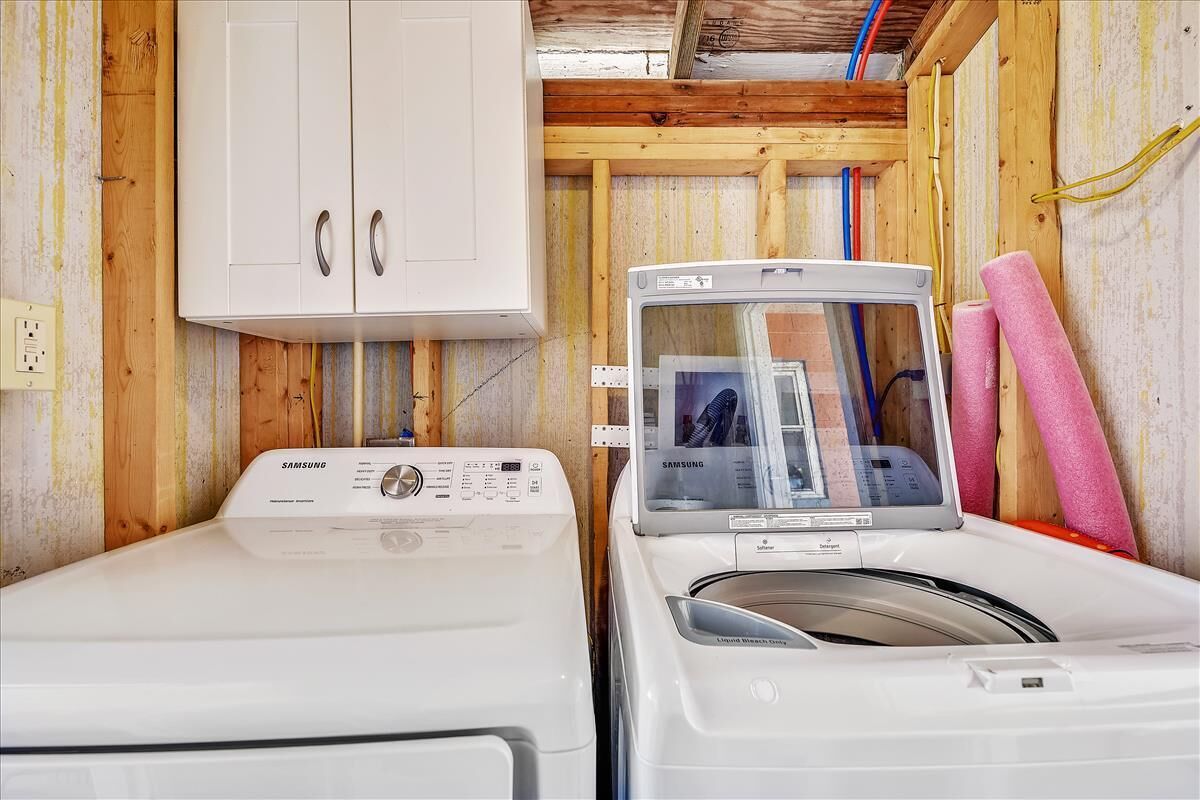 A laundry room with two white Samsung washing machines, a white cabinet, and wooden walls.