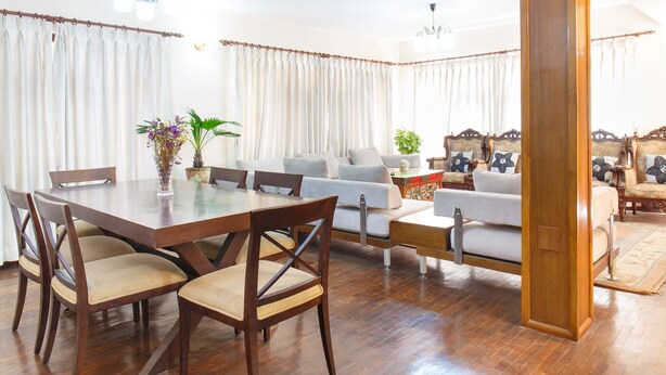 Een ruime woonkamer met een houten eettafel, lichte banken en een grote houten zuil.