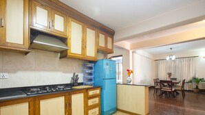 Een keuken met houten kastjes, een blauwe koelkast, een gasfornuis en een eethoek met een tafel en stoelen.
