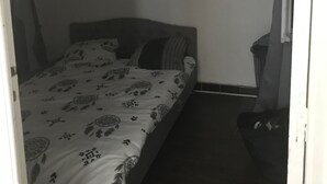 Una habitación pequeña y con poca luz, con una cama individual, una mesita de noche y un cubo de basura.