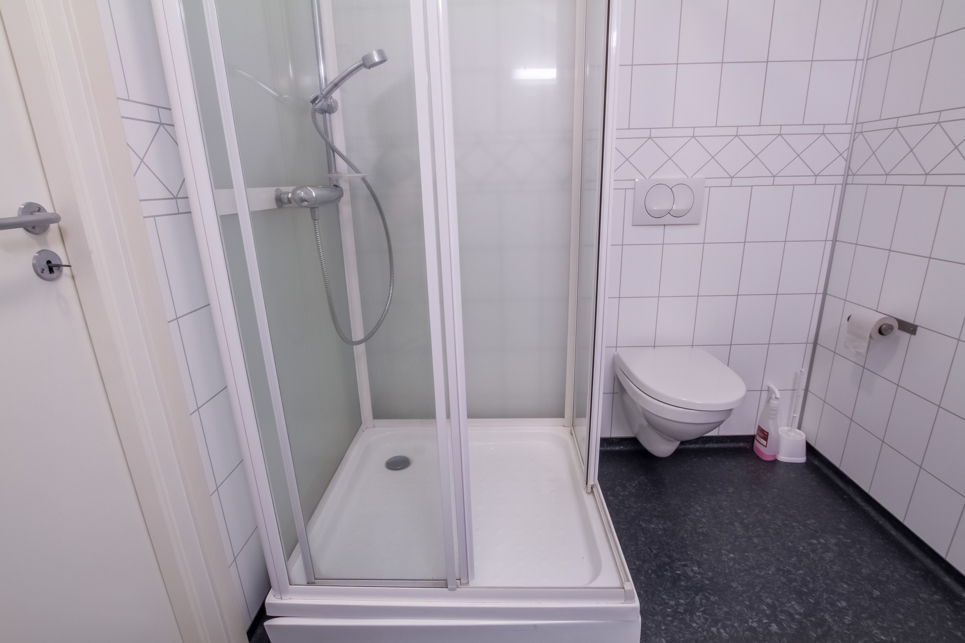 A small, enclosed shower area with a glass door, a white toilet, and a black floor.