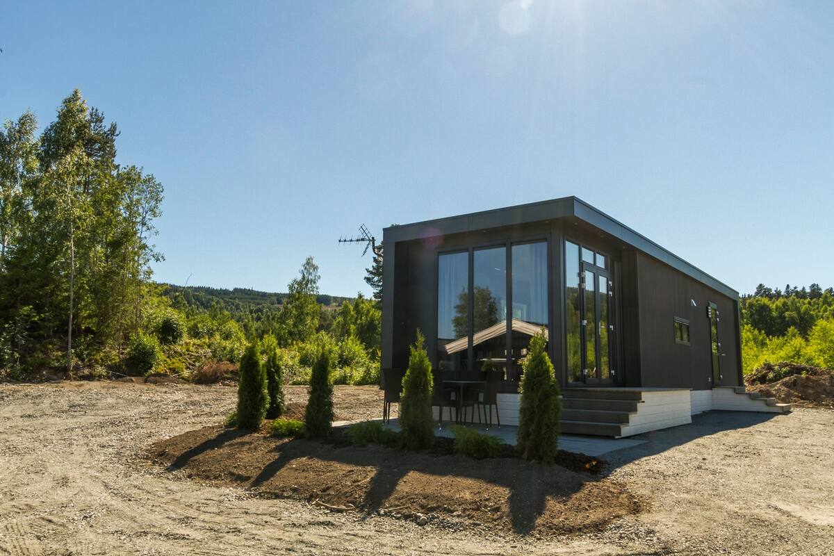 Une maison moderne dotée de grandes fenêtres, d’une terrasse en bois et d’une allée non pavée.