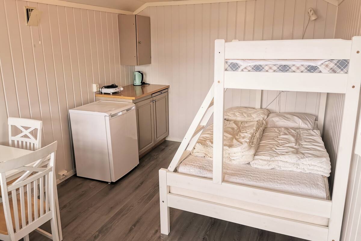 Une pièce compacte comprenant un lit superposé, une petite kitchenette, un lave-linge et une chaise blanche.