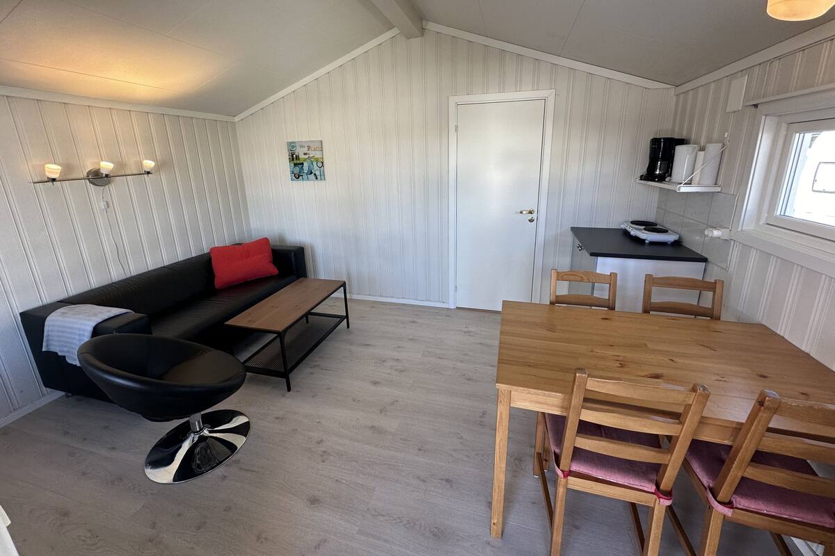 Un espace de vie compact comprenant un canapé, une table à manger avec des chaises, un banc et un petit coin cuisine équipé d’une machine à café.