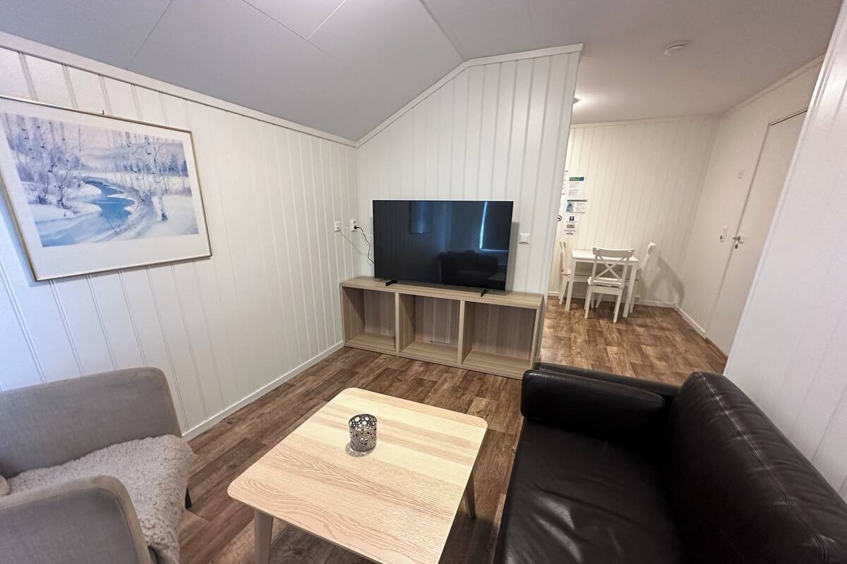 Un salon avec un téléviseur, une table basse en bois, un canapé en cuir noir et un tableau accroché au mur.