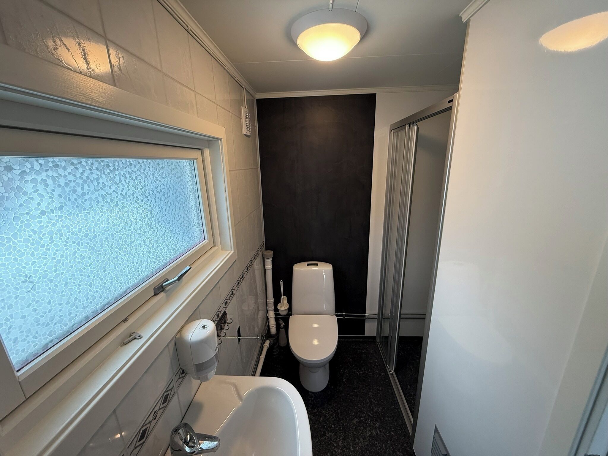 Un baño pequeño con inodoro, lavamanos y ventana con vidrio esmerilado.