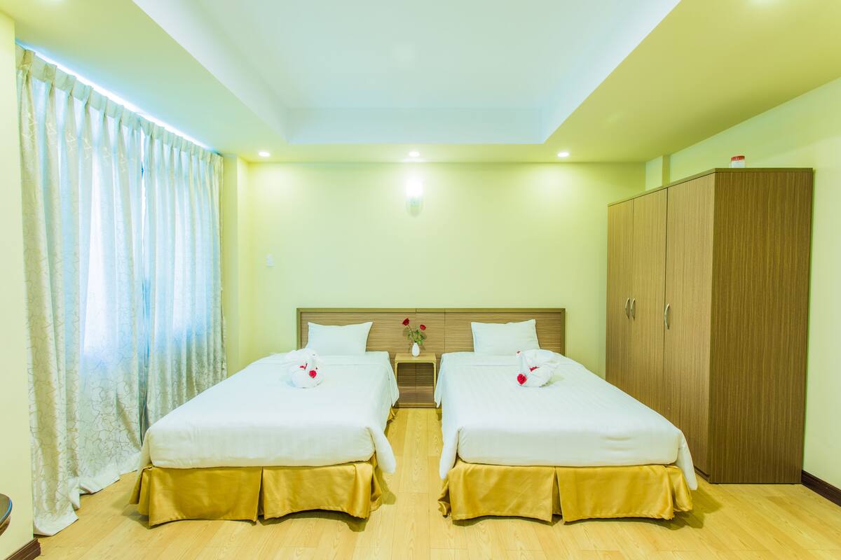 A hotel room with two beds, a wardrobe, and a nightstand with a vase of flowers.