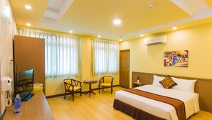 A hotel room with a bed, a desk with a telephone, two chairs, a small table, and a painting on the wall. - Golden Gate China Town Hotel (Yangon)