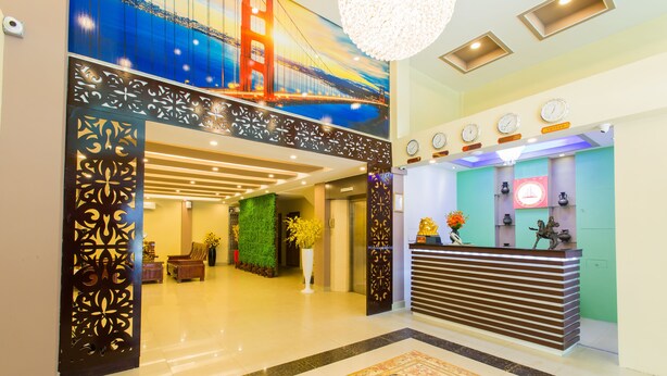 A hotel lobby with a reception desk, decorative panels, a large clock, and a mural of a bridge. - Golden Gate China Town Hotel (Yangon)