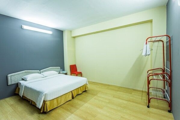 A bedroom with a bed, a red chair, and a metal rack with a towel. - Golden Gate China Town Hotel (Yangon)