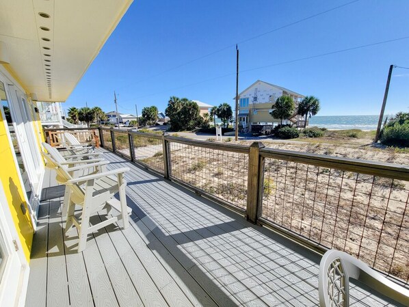 A wooden deck with white chairs, a railing, and a view of the beach and ocean.
