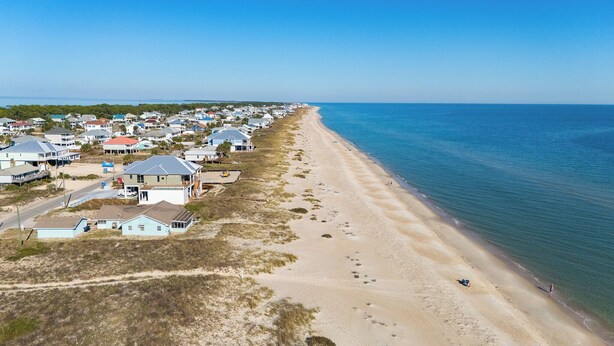 Eine Vogelperspektive auf eine Küstenwohngegend mit Häusern entlang des Strandes, klarem Himmel und ruhiger See.