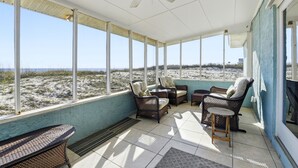 Eine überdachte Terrasse mit Korbmöbeln, großen Fenstern und einem Deckenventilator.