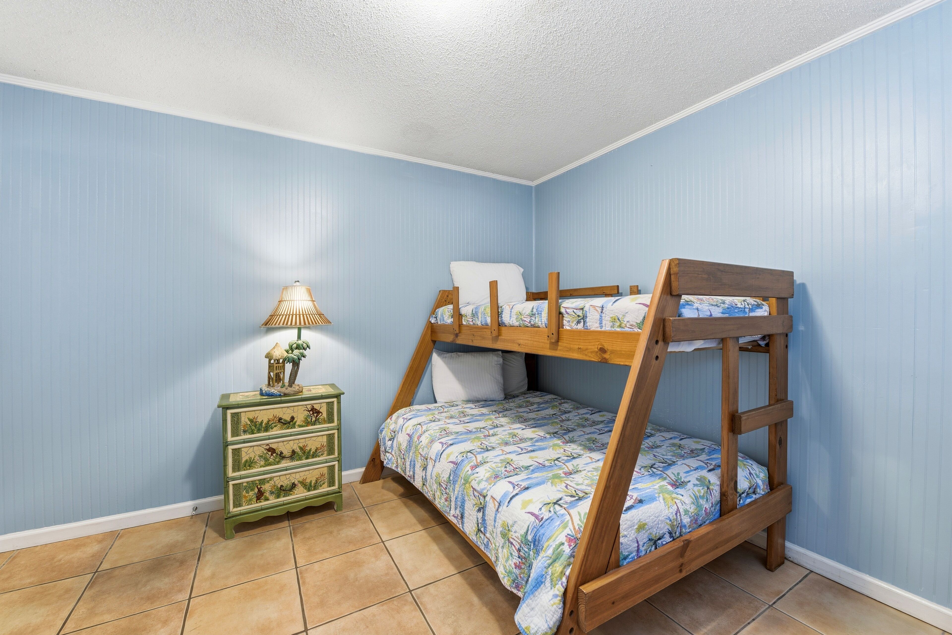 A bunk bed with a floral bedspread, a green nightstand with drawers, and a lamp.