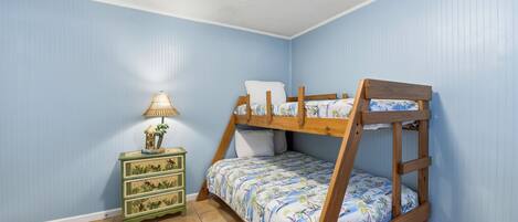 A bunk bed with a floral bedspread, a green nightstand with drawers, and a lamp.