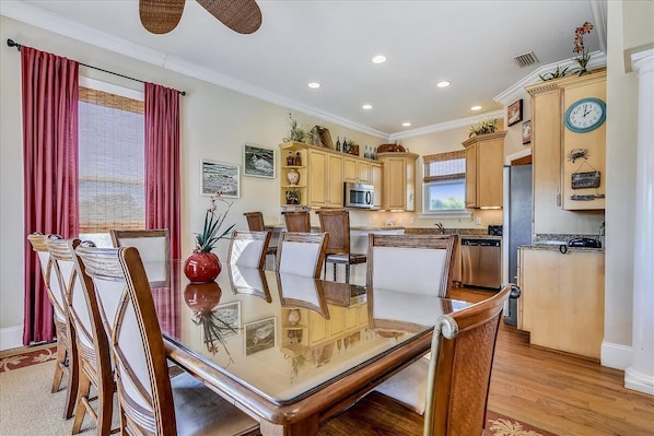 A dining area with a glass table and wooden chairs, a kitchen with wooden cabinets and appliances, and a clock on the wall. - CREATE THE PERFECT VACATION experience for the whole family in Pretty Woman! (St. George Island)