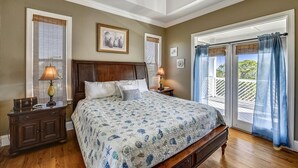 A bedroom with a large bed, wooden headboard, two bedside tables with lamps, and a view of a balcony through a sliding glass door. - CREATE THE PERFECT VACATION experience for the whole family in Pretty Woman! (St. George Island)