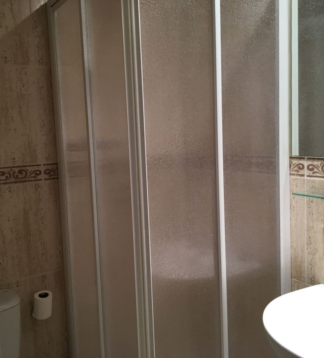A bathroom with a shower enclosure, a toilet, and a sink.