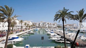 Ein Yachthafen mit zahlreichen vertäuten Booten, umgeben von Palmen und Gebäuden im mediterranen Stil.