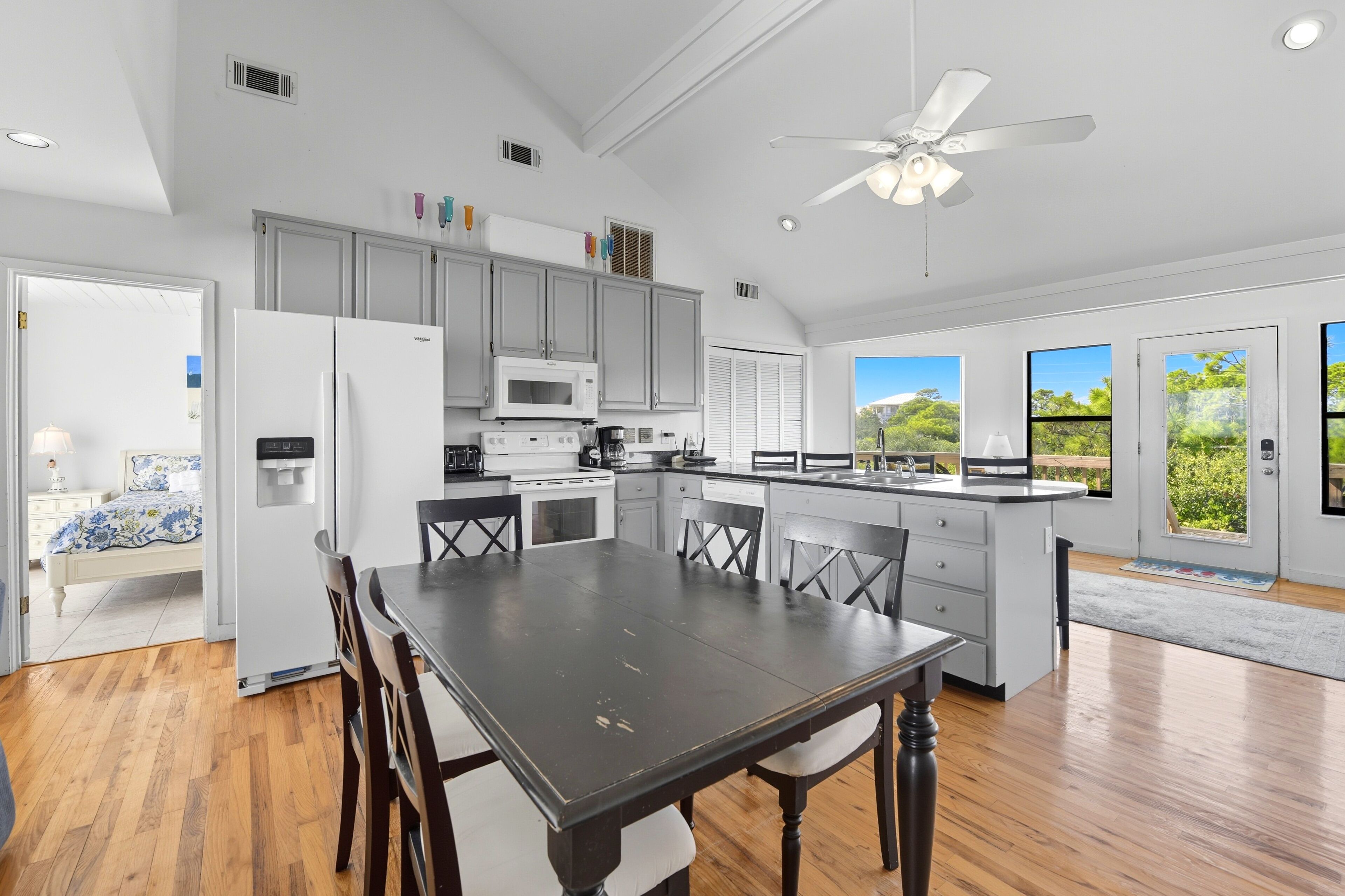 A modern kitchen with white cabinets, a large island, and a dining area with a dark wooden table and chairs.