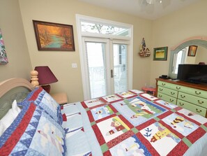 Un dormitorio con cama, cómoda, televisor y ventana con persianas.