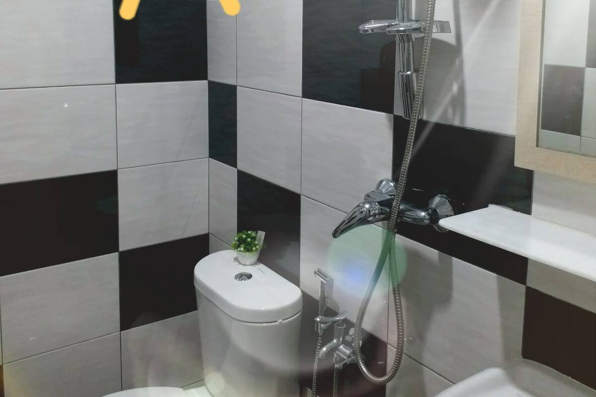 Une salle de bain avec un mur recouvert de carreaux noirs et blancs formant un motif à damier, des toilettes, un bidet et un lavabo.