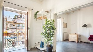 Un salon lumineux avec un balcon, une plante en pot, un bureau en bois et une chaise rouge.