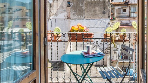 Un balcon avec une table bleue, des plantes en pot et une vue sur les immeubles voisins.