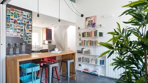 Une cuisine moderne avec un plan de travail en bois, des tabourets de bar, une bibliothèque et un mur recouvert de photos.