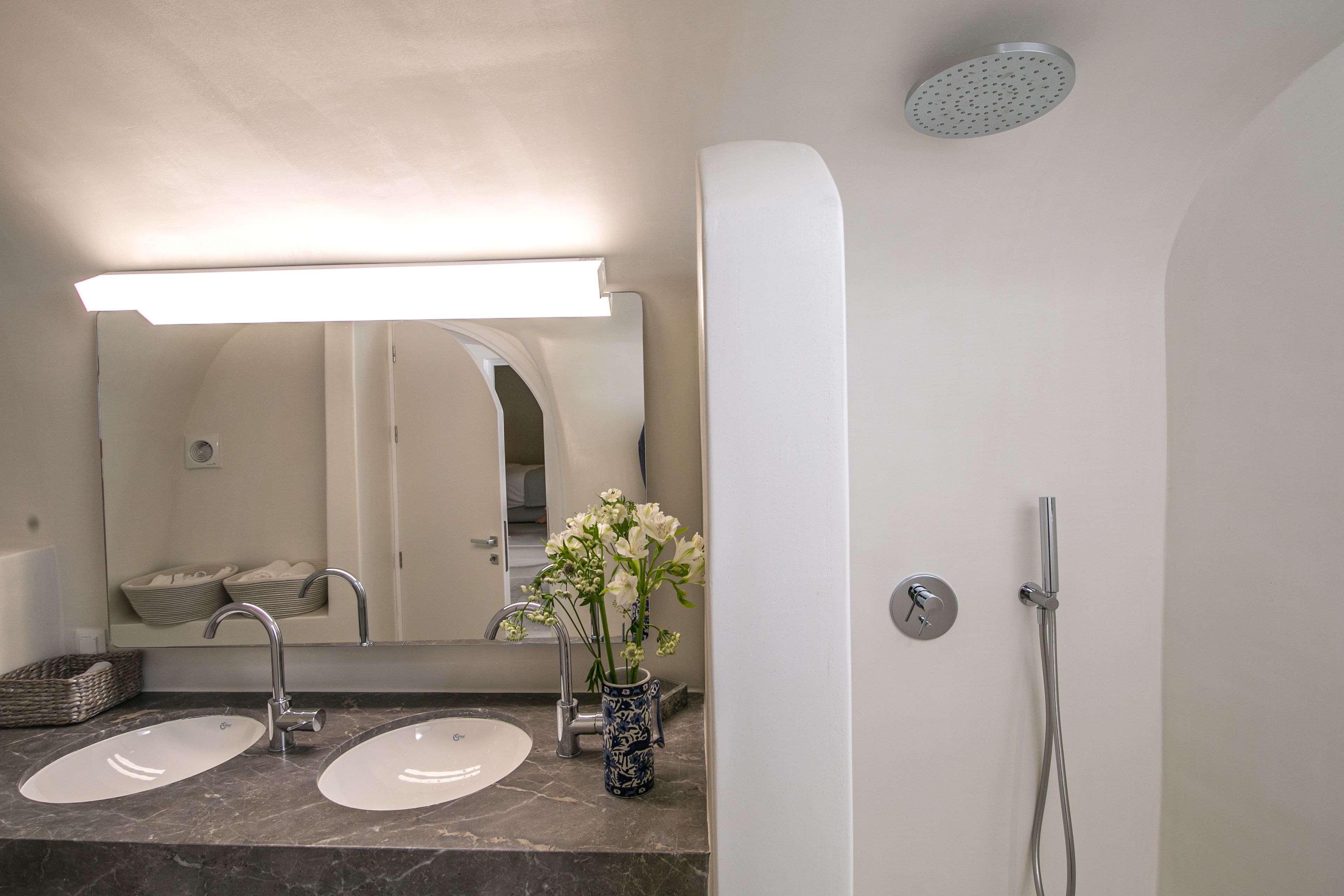 Une salle de bain avec deux lavabos, un miroir, une douche et un vase de fleurs.
