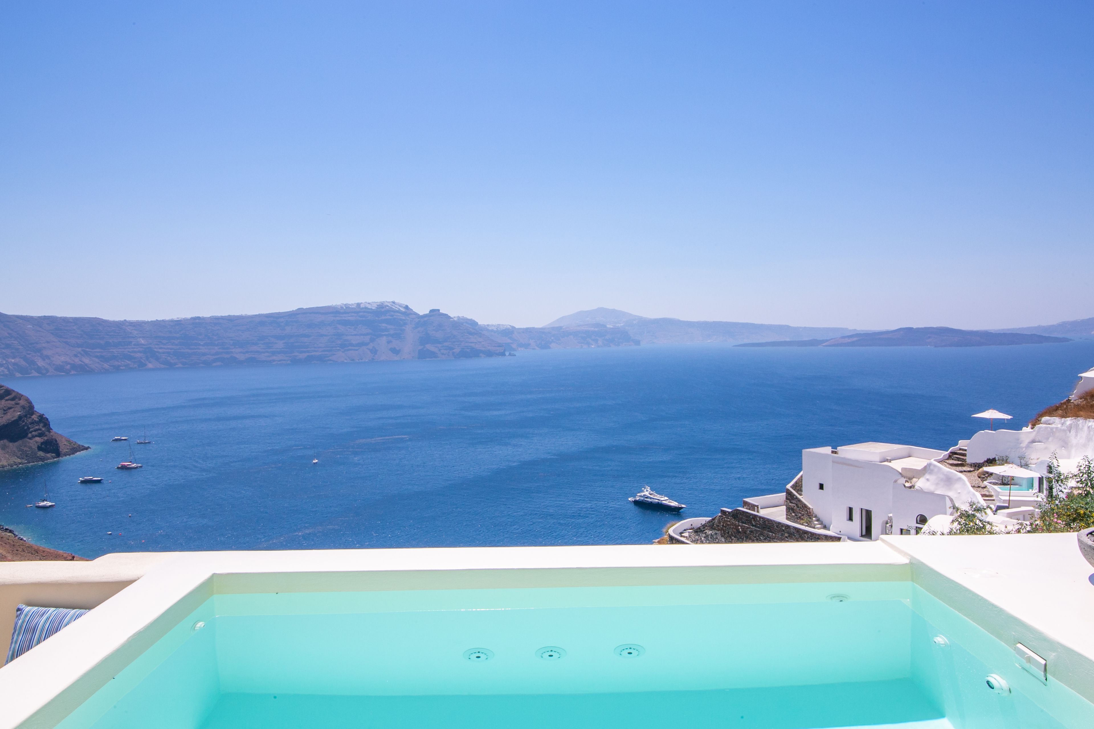 Vista despejada de una gran piscina azul claro con vistas al mar y edificios blancos al fondo.