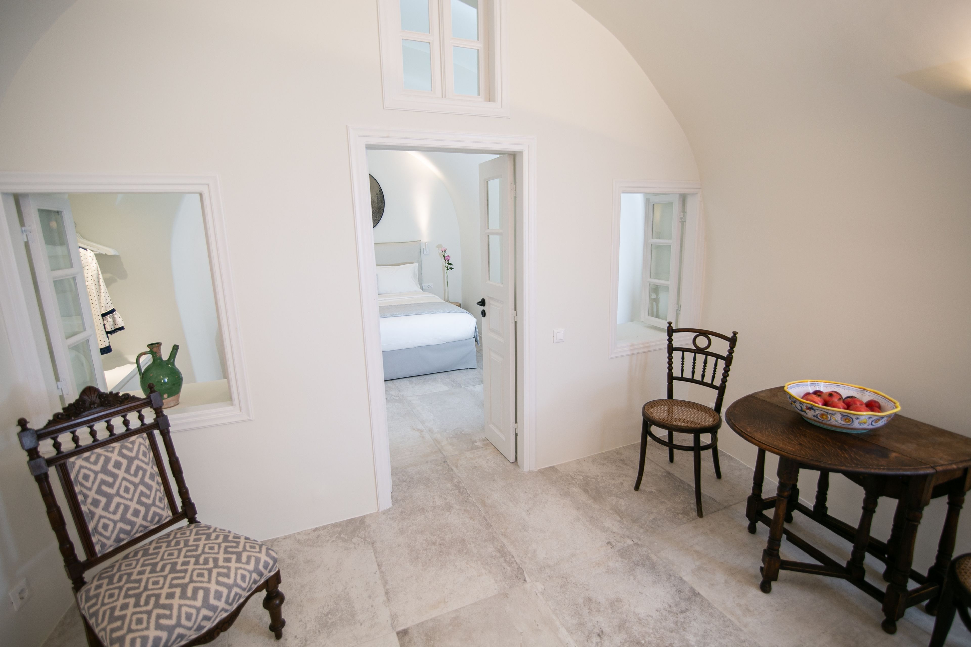 A room with a dining table, two chairs, a bowl of fruit, and a bed in the background.