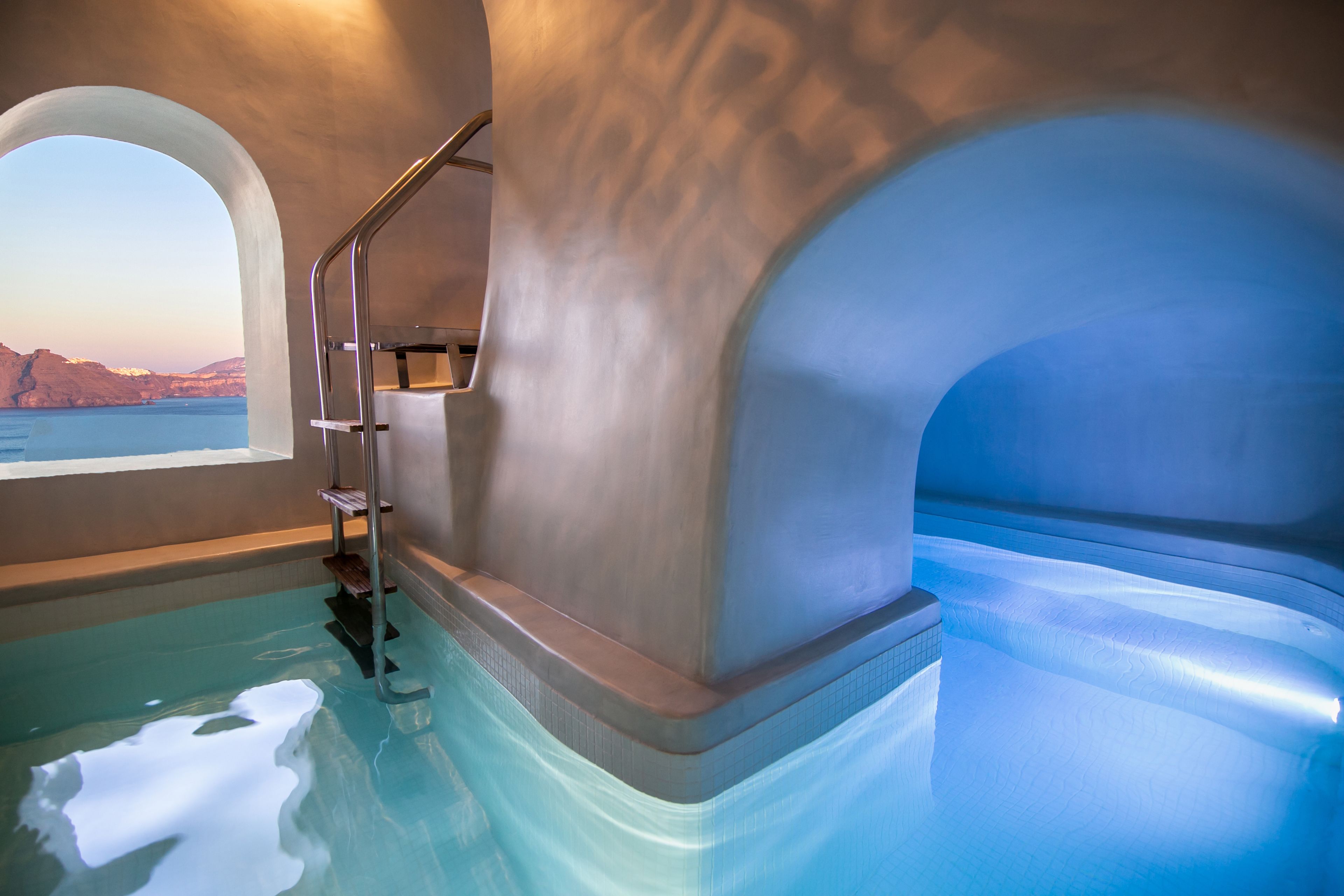 A modern indoor pool with clear blue water, a view of the sea, and a staircase leading to an upper level.
