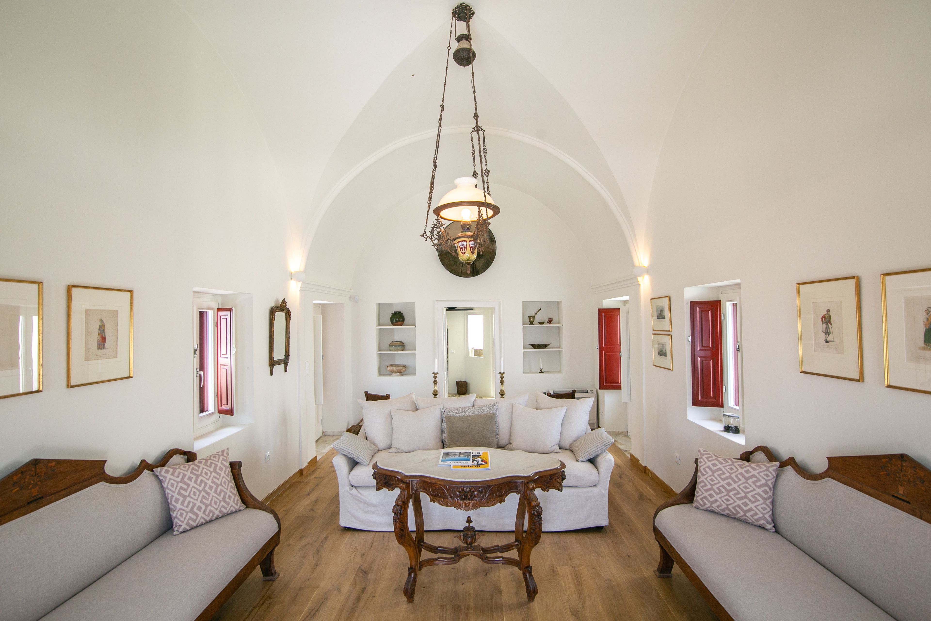 Un vaste salon doté d’un haut plafond en arc de cercle, d’un canapé blanc placé au centre, d’une table basse en bois et d’une lampe suspendue.
