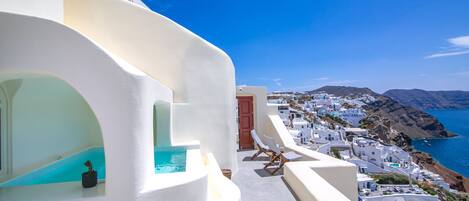 A white-walled building with a pool, a door, and a view of a coastal town.