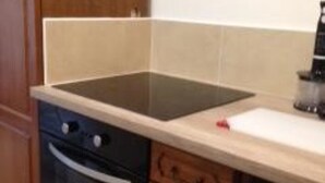 A kitchen with wooden cabinets, a black oven, a white countertop, and a black induction cooktop. - Quiet and bright apartment near the shops (Berck)