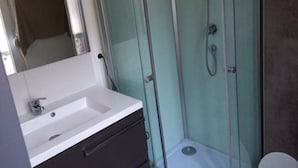 A bathroom with a glass-enclosed shower, a sink, and a mirror. - Quiet and bright apartment near the shops (Berck)