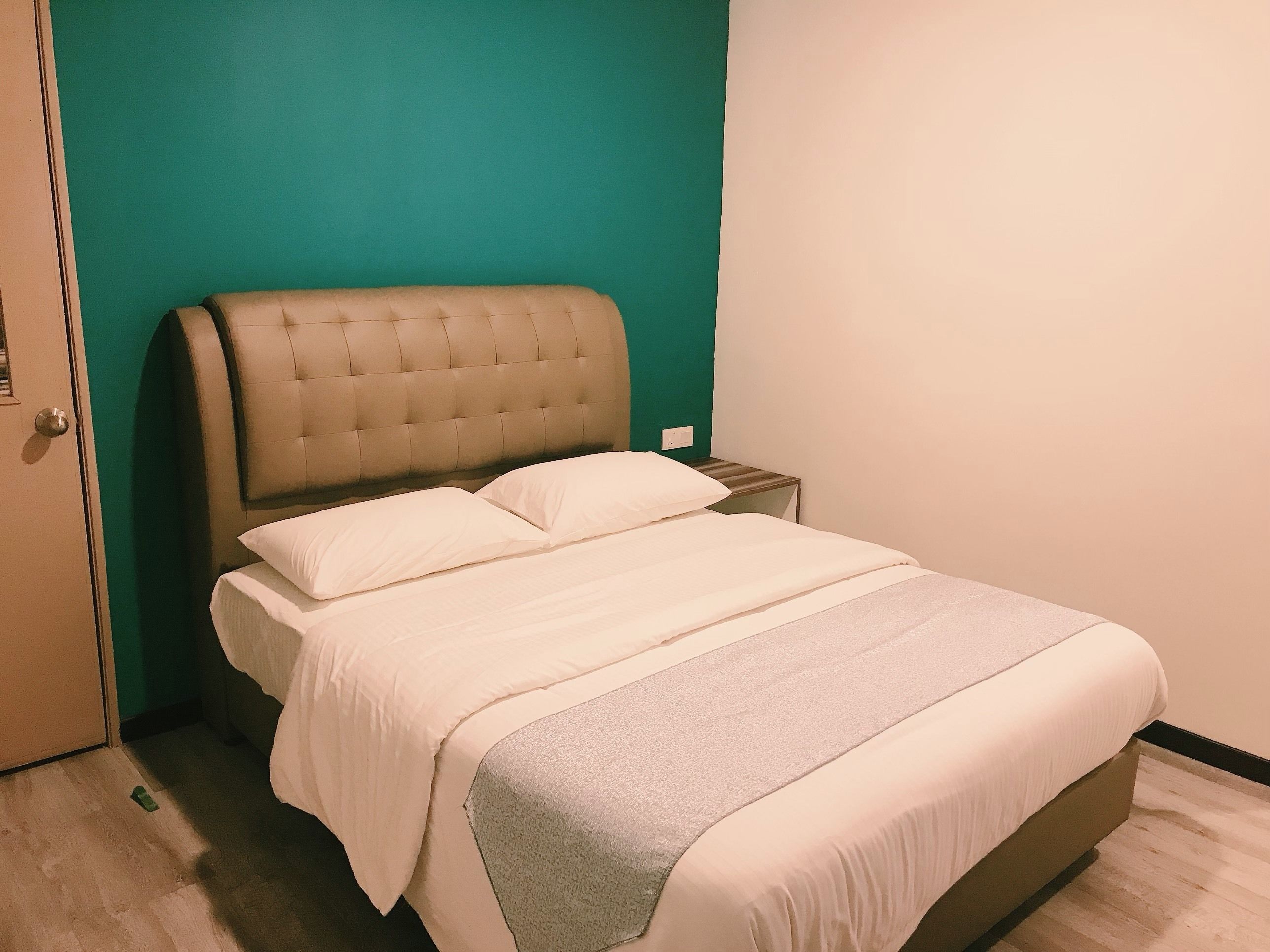A bed with a tufted headboard, two pillows, and a grey throw blanket.