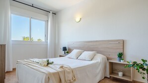 A bedroom with a large bed, bedside tables, a nightstand, a wall-mounted light, and a window with curtains. - LOS RISCOS 2 (La Pineda)