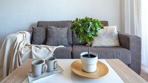 A living room with a grey sofa, a small potted plant, a coffee table with two mugs, and a white tablecloth. - LOS RISCOS 2 (La Pineda)