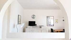 Een minimalistisch ingerichte kamer met een wit gewelfd plafond, een klok aan de muur, een flatscreen televisie op een kast en een lijst met een afbeelding.