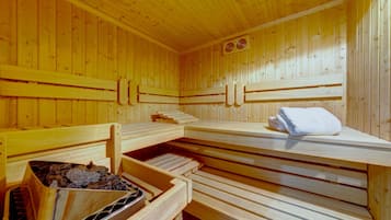 En sauna med træbænke, et håndklæde på en bænk og en bakke med sten og en skål.