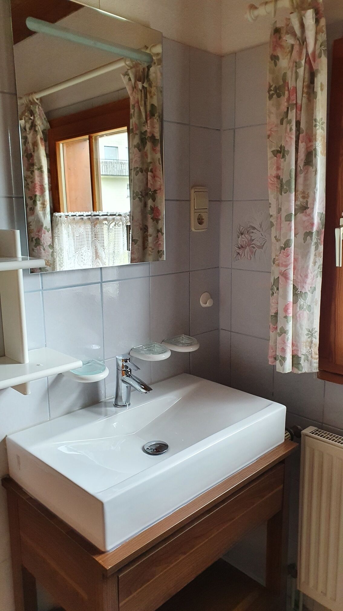 Uma casa de banho com uma pia branca, um espelho e um chuveiro com cortina estampada com flores.