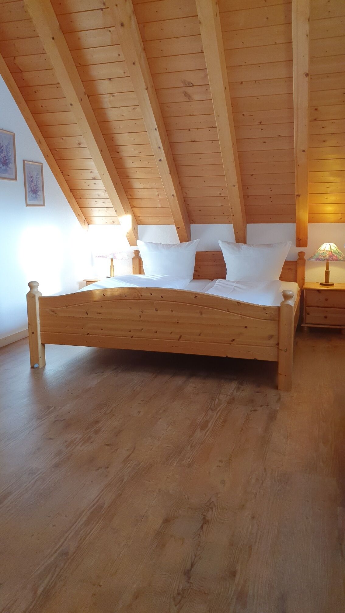 Una cama de madera en una habitación con techo inclinado y vigas de madera.