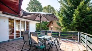 Une terrasse avec une table et des chaises, un parasol et une vue sur une maison et des arbres.