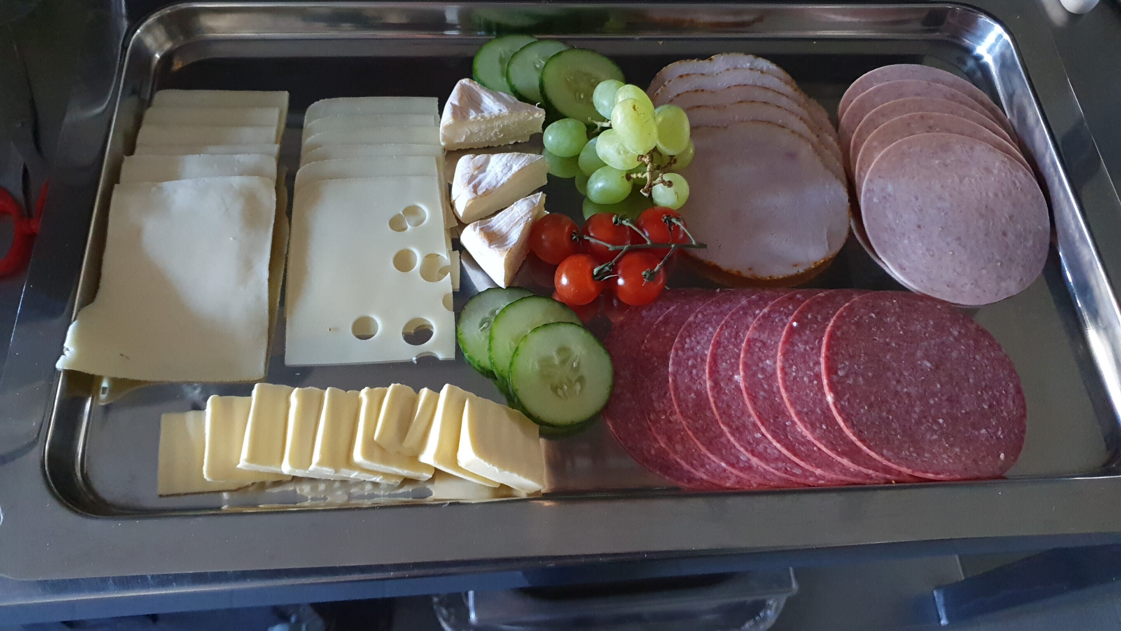 Eine Platte mit verschiedenen Aufschnittwaren, darunter Schinken, Salami, Käse, Trauben und Kirschtomaten.