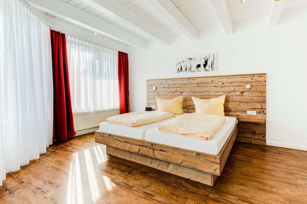 A bedroom with a wooden bed frame, white bedding, and a red curtain.
