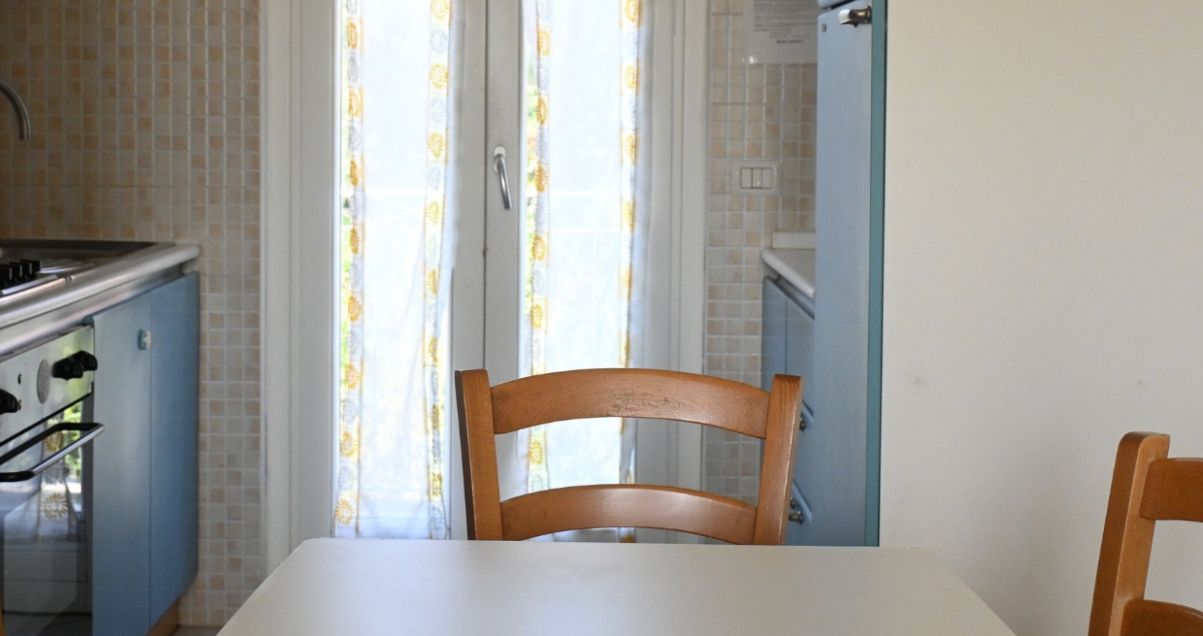A kitchen with a stove, sink, and cabinets. There is a wooden chair at a table.