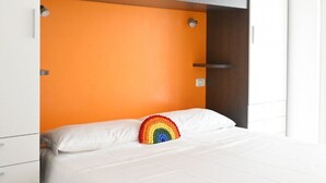 A bed with a rainbow-patterned pillow, white bedding, and an orange headboard. - N148 - Numana, new three-room apartment with terrace 350mt from the sea (Numana)